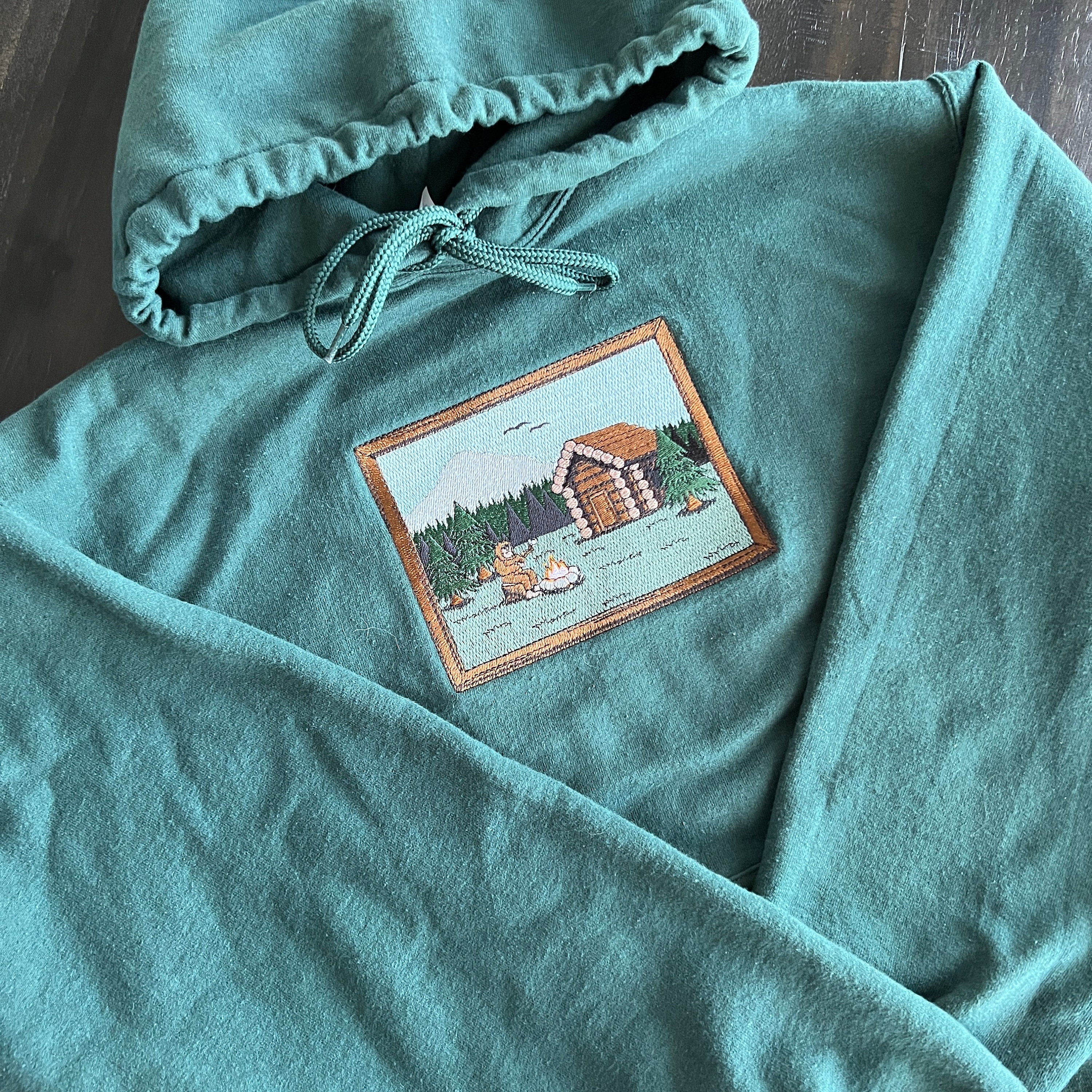 Sasquatch Log Cabin Scene Embroidered Hoodie Sweatshirt Unisex Camping Forest Mountains Long Sleeve Outdoors Personalized Multiple Colors